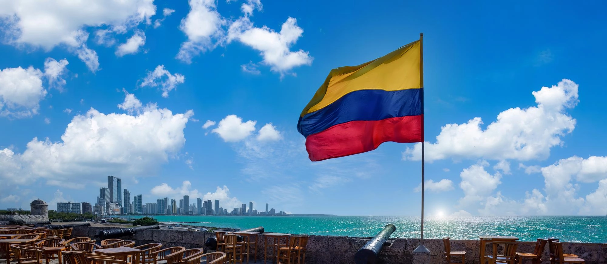 Bandera de Colombia frente al mar Caribe con vista urbana costera, uno de los destinos inolvidables para visitar